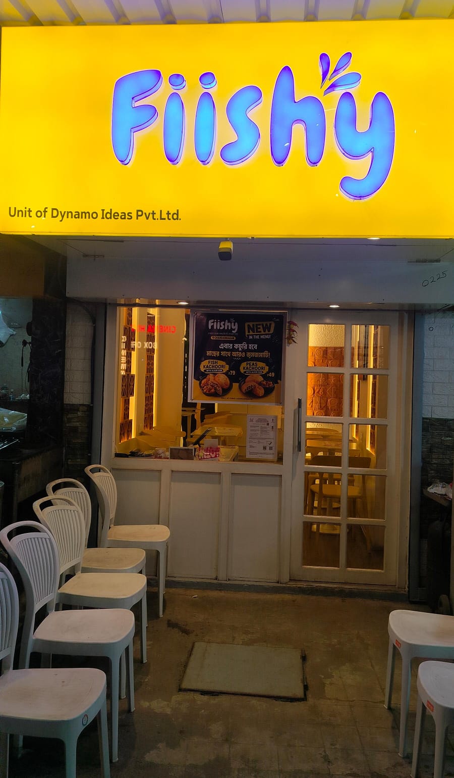 The Chandannagar shopfront, blue neon on a yellow board with pavement seating below