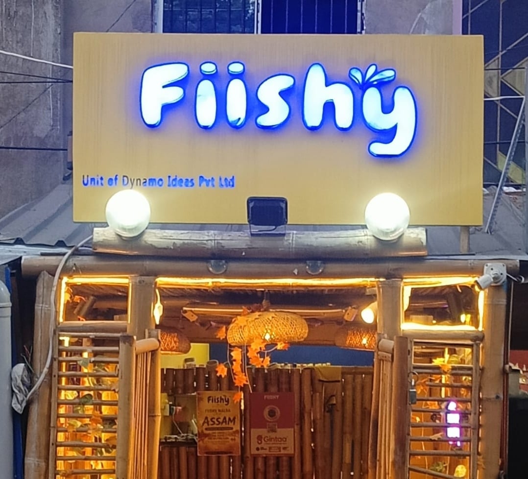 A fish fry with onion and kasundi held up under the neon fish sign at Malda