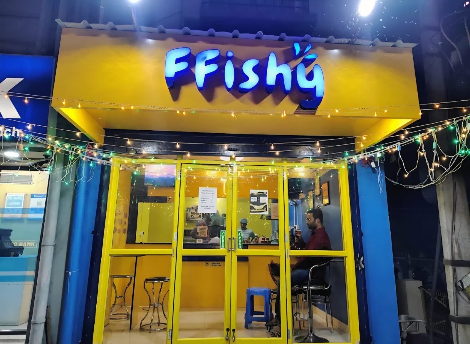 The Bardhaman counter at night, fairy lights strung across a yellow shopfront