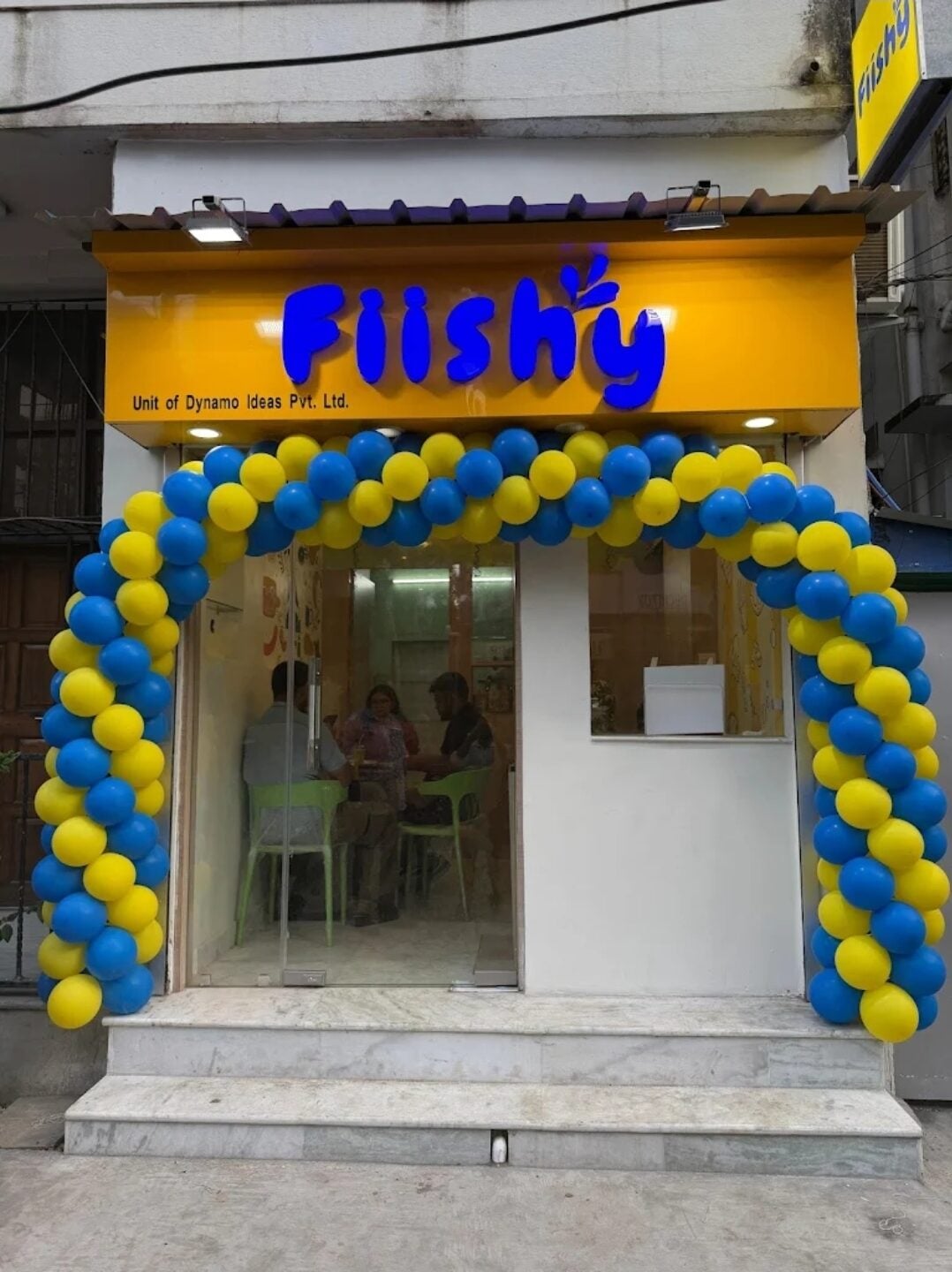 The Lake Town shopfront on opening day, yellow board and a blue and yellow balloon arch